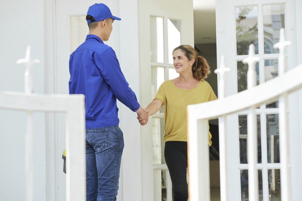 Smiling woman shaking hands with HVAC technician in uniform while he stands outside her front door.